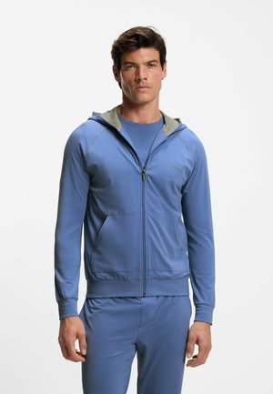 Blå zip-up hoodie med en grå innervadding, med framfickor och en slät textur. Bärs över en matchande blå skjorta.