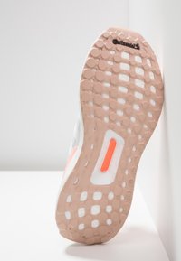 Podeszwa buta z teksturowanym wzorem zawierającym okrągłe elementy. Kolorystyka: różowy, biały i pomarańczowe akcenty. Widoczne logo "Continental".