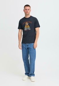 Camiseta gris oscuro con un diseño impreso que presenta una figura de dibujos animados, combinada con unos jeans de mezclilla azul claro y zapatillas blancas.
