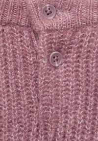 Gros plan sur un tissu en maille rose poussiéreux avec deux boutons transparents roses et des fibres texturées visibles.