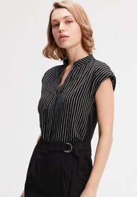 Chemise noire à col avec des rayures verticales blanches, manches courtes retroussées et patte de boutonnage, assortie à un pantalon noir taille haute.