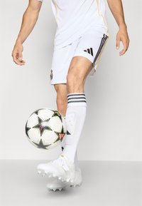 Uniforme da calcio bianco con accenti gialli, strisce nere sui pantaloni e scarpe bianche. Presenta un pallone da calcio con un motivo in bianco e nero.
