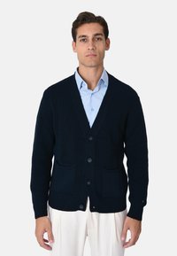 Cardigan lavorato a maglia blu navy con scollo a V, sei bottoni e due tasche frontali. Polsini e orlo a costine, realizzato in tessuto strutturato.