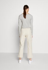 Světle šedý dlouhý rukáv s výstřihem do lodičky, kombinovaný s krémovými širokými kalhotami, modelovaný s bílými teniskami, pohled zezadu.