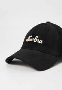 Melna korduroja beisbola cepure ar izšūtu "New Era" logo krēmbālā. Iespējas ietver izliekto attēlu un regulējamu siksnu aizmugurē.