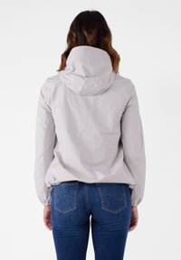 Giacca leggera grigio chiaro con cappuccio, polsini elastici e orlo con cordino. Indossata con jeans in denim blu. Tessuto liscio e texture.