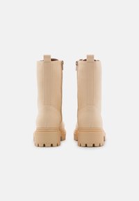Bottes chelsea couleur beige avec une finition textile lisse, dotées d'une semelle épaisse, d'une fermeture éclair latérale et de deux languettes en haut.