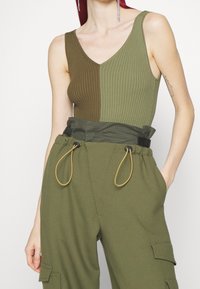 Bodycon a coste in verde oliva con pannelli in verde oliva scuro, abbinato a pantaloni cargo khaki con cordini regolabili e dettagli delle tasche.