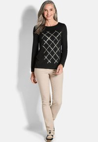 Schwarzes Longsleeve-Oberteil mit einem Diamantmuster aus silbernen Akzenten. Kombiniert mit beigen, geraden Hosen und schwarz-beigen Sneakers.