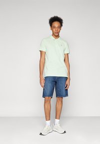 Lysegrønn bomullspolo, denimshorts, hvite joggesko med grå detaljer. Enkelt design, kortermet, logo på brystet.
