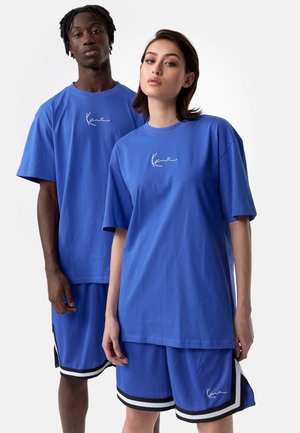 Bright blue oversized t-shirts paired with matching blue shorts featuring white and black stripes. Each shirt has a simple white logo.