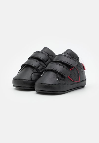Sapatos de couro pretos para crianças pequenas, com duas tiras de Velcro, biqueira redonda, parte superior texturizada e um pequeno destaque vermelho perto do logótipo.