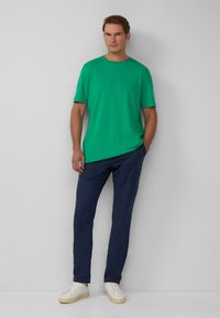 Zielona koszulka krótki rękaw z okrągłym dekoltem, zestawiona z ciemnoniebieskimi lekkimi spodniami i białymi trampkami z beżową podeszwą.