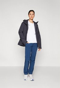 Wodoodporna, ciemnoszara kurtka z kapturem, biała koszulka i niebieskie spodnie. Model nosi białe trampki. Prosty, funkcjonalny design.