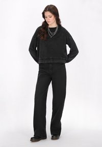 Felpa nera corta con una finitura testurizzata, abbinata a jeans neri a vita alta e a gamba larga. Gli accessori includono catene d'argento a strati.