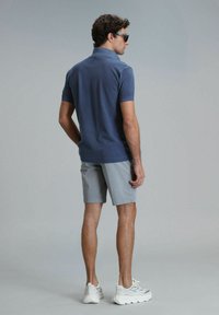 Dunkelblaues Poloshirt mit kurzen Ärmeln, kombiniert mit hellgrauen Shorts. Die Person trägt Sonnenbrillen und weiße Sneakers.