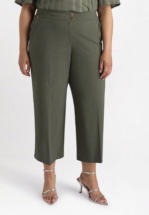 Pantaloni a culotte verde oliva con due bottoni frontali, caratterizzati da una trama liscia e un design su misura, abbinati a tacchi a strisce argento.