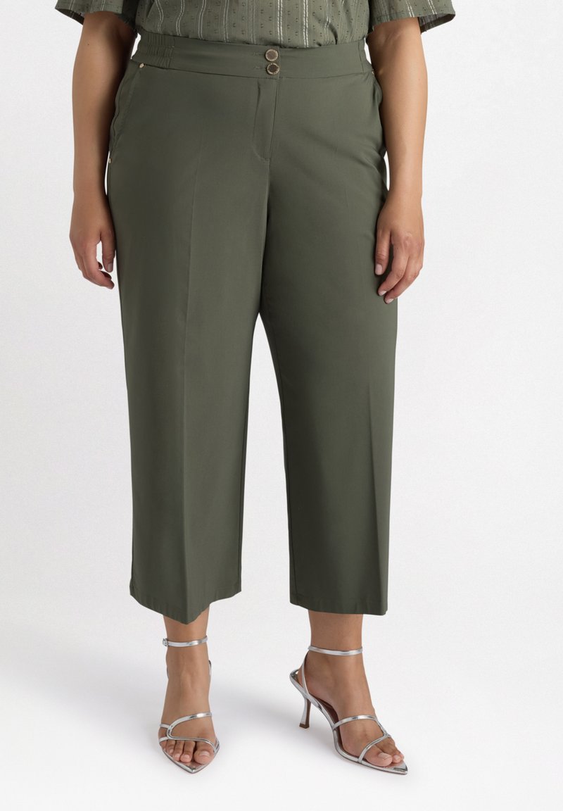 Pantalons cropped vert olive avec deux boutons à l'avant, présentant une texture lisse et un design ajusté, associés à des talons aiguilles argentés à lanières.