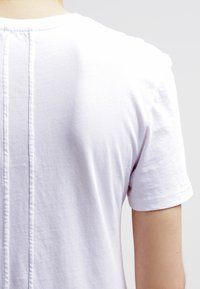 Vit bomulls T-shirt med rund hals, korta ärmar och vertikala sömmar längs ryggen. Slät textur utan synliga mönster.