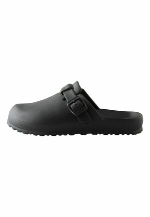 Schwarzer Slip-On-Clog mit strukturierter Sohle und verstellbarem Riemen mit quadratischer Schnalle, seitlich auf weißem Hintergrund dargestellt.