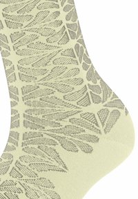 Sekcja skarpet z beżowej tkaniny z jasnoszarym, abstrakcyjnym wzorem liści dzianym na całej powierzchni.