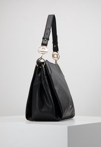 Černá kožená kabelka s hladkou texturou, měkkým tvarem, zlatými kovovými doplňky a nastavitelným popruhem s kruhovými detaily.