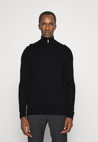 Suéter preto de mangas longas com fecho de correr, feito de material suave, apresentando um design ajustado e uma sutil textura canelada nos punhos e na bainha.