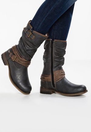 Bottes en cuir noir hautes avec des sangles et boucles marron. Présentent une fermeture éclair sur le côté et une finition texturée. Talon bas en bloc.