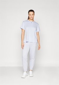Ljust grå t-shirt med kort ärm och rund hals, med en diskret logotyp, matchad med tapered sweatpants i samma färg och vita sneakers.