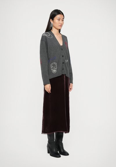 Grijs wollen cardi met kleurrijke geborduurde details, zwarte knopen, gedragen over een bordeaux fluwelen rok en zwarte enkellaarsjes met hak.