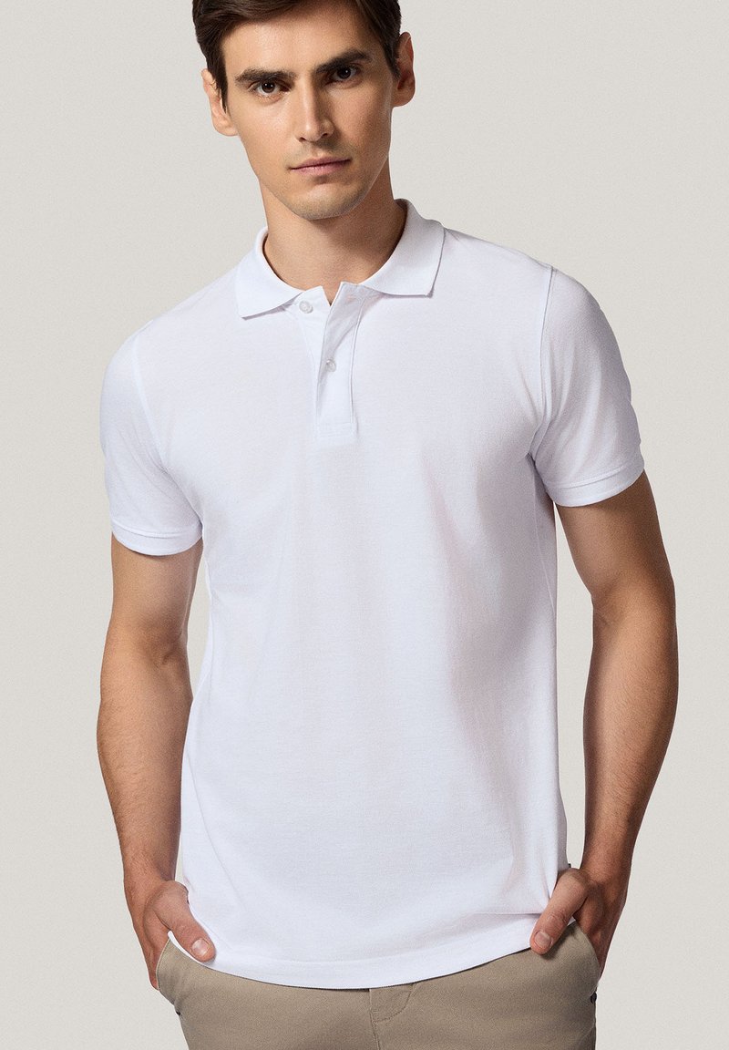 Biała koszulka polo wykonana z bawełny, z kołnierzykiem i krótkimi rękawami. Prosty design z zapięciem na guziki. Gładka faktura.