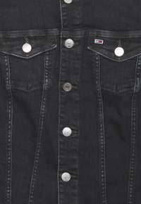 Black denim jacket featuring silver snap buttons, two chest pockets, and a small branded logo on the left pocket. Textured fabric, structured design.