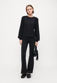 Black knit sweater with ribbed texture and puffed sleeves, paired with fitted black flared pants and chunky black shoes, holding a small bag.