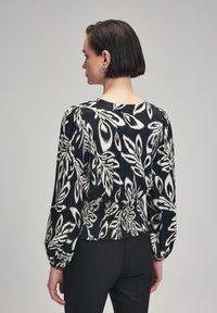 Sorte og hvide bluse med blomstermønster, med en figursyet smocket talje og lange puffærmer. Glat stof med en let tekstur.