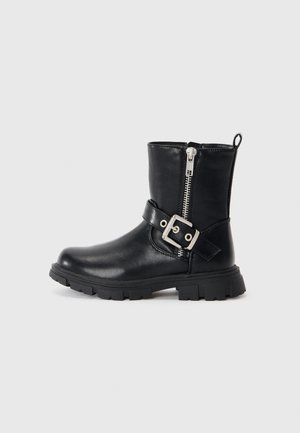 Botte en cuir noire mi-mollet avec semelle épaisse, fermeture éclair latérale et bride décorative à boucle autour de la cheville sur un fond uni.