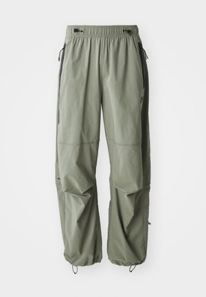 Jasnooliwkowe spodnie cargo z elastycznym pasem, regulowanymi mankietami i czarnymi kieszeniami bocznymi, prezentowane na białym tle.