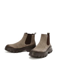 Bottes de cheville en daim marron avec panneaux élastiques latéraux, semelles en caoutchouc épaisses et languettes de traction pour un enfilage facile. Texture lisse et conception robuste.