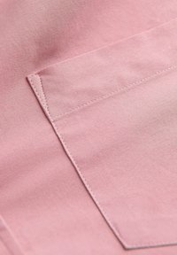 Roze stoftextuur met een zak met nauwkeurige stiksels en een gladde oppervlakte, die de nadruk legt op een schoon ontwerp en een zachte uitstraling.