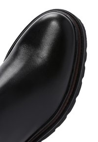 Close-up van de gladde zwarte leren schoenpunt met dikke zwarte rubberen zool en bruine stiknaad.