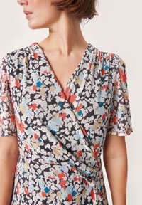Vestido envolvente floral en tela ligera, con un fondo negro decorado con flores blancas, rojas, azules y beiges. Mangas cortas abullonadas.