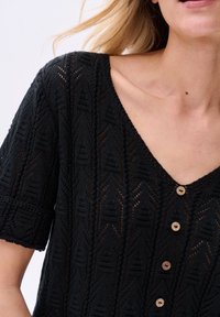 Czarny dzianinowy top z dekoltem w serek, krótkimi rękawami i drewnianymi guzikami. Posiada wzory ażurowe i fakturowe detale na całej powierzchni.