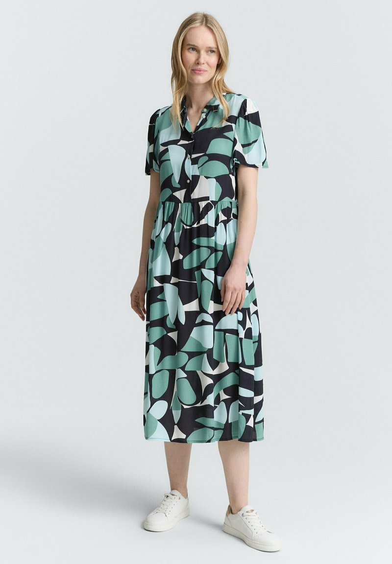 Robe boutonnée à manches courtes, présentant un motif abstrait vert, noir et blanc, taille cintrée et une jupe fluide de longueur mi-mollet.