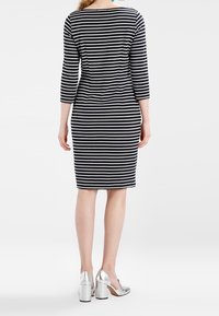 Schwarz-weiß gestreiftes Kleid mit Dreiviertelärmeln, figurnahes Design, knielang. Modell trägt silberne High Heels.