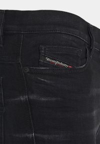 Svarta jeans i denim med en texturerad yta, med en liten fickdetalj och en "Diesel"-etikett sydd i röd och vit.