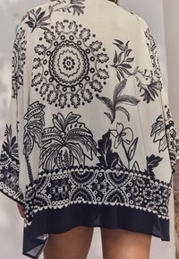 Mustat ja valkoiset kukkakuosiset ja geometriset kuviot sisältävä kimono, kevyt kangas, löysä muotoilu ja kaareva helma.