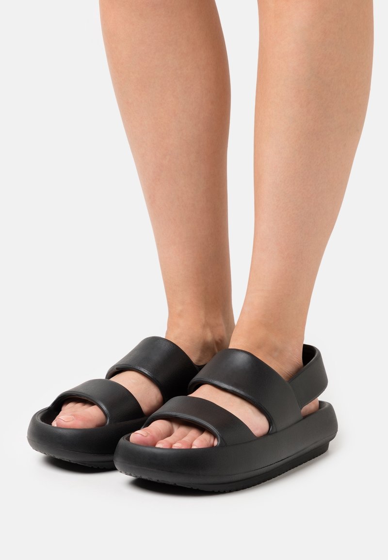 Sandales noires avec larges brides, design à bout ouvert et semelle texturée. Fabriquées en matériau synthétique avec une finition lisse et mate.