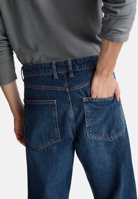 Tmavě modré džíny s uvolněným střihem, s zadními kapsami, pásem a texturovanou tkaninou. Viditelné švy accentuují.