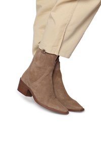 Rudos suede aulinukai iki kulkšnies su smailiu nosiu, dekoratyvine siuvinėjimo linija ir storu kulnu, derinami su šviesiai beige kelnių.