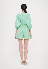 Zaļgans un zilgans svītrots īss rompers ar pūkainām piedurknēm, jostu viduklī un brīvu piegriezumu. Gluda auduma ar vieglu tekstūru.