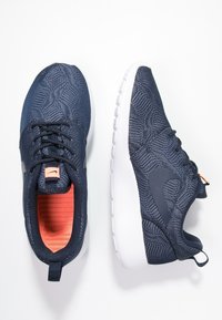 Marineblaue Sportschuhe mit einer strukturierten Oberseite, orangefarbenem Innenfutter, weißer Sohle und dezenter Logodetails an der Seite.